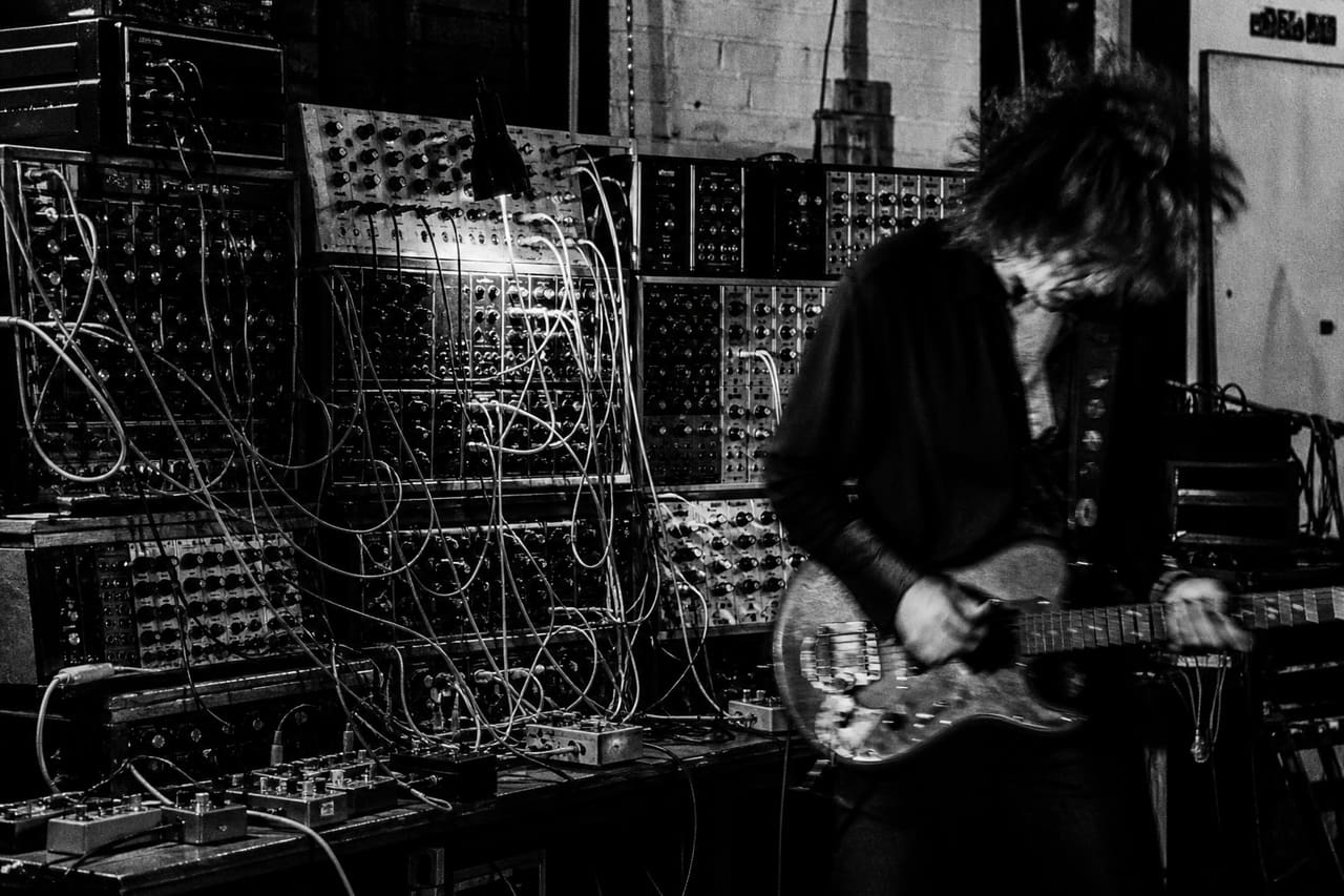 Musician Performing with an Electric Guitar and Synthesizer in a Dark Studio